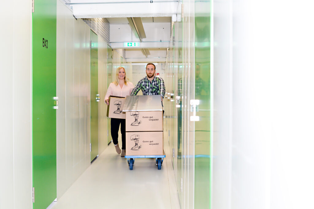 Kunde transportiert Umzugskartons auf Rollwagen durch die Lagerboxen von Packsweg Self Storage in Stuttgart